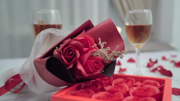 一束鲜花，盒子里的玫瑰躺在浪漫晚餐的桌子上，两杯酒。