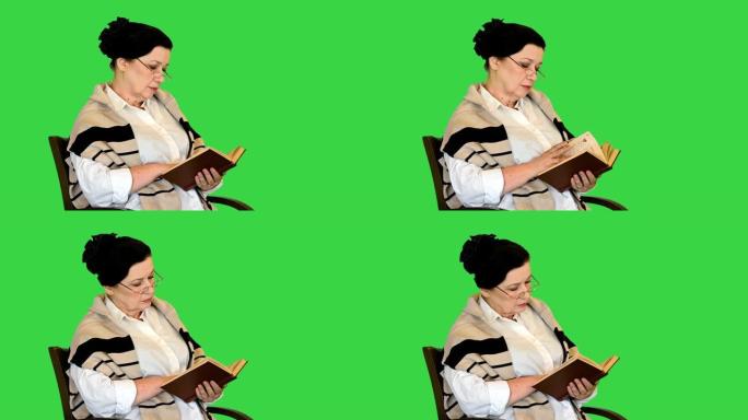 友好的高级妇女坐在椅子上阅读绿屏上的书，色键