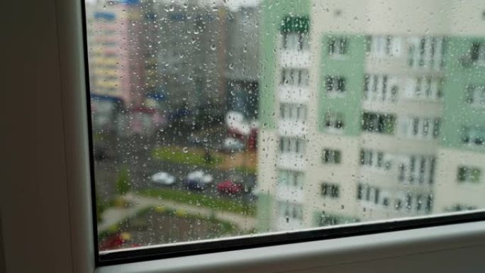 雨滴在窗户玻璃上观看城市景观。带有建筑物背景的窗玻璃上的雨滴。窗户上下雨的风景。