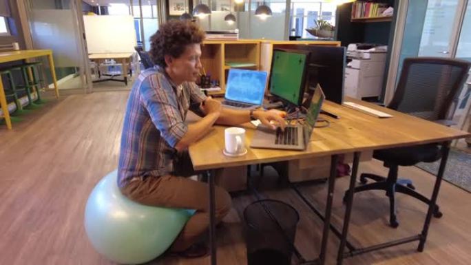 IT专业程序员坐在瑜伽球上玩压力球检查屏幕