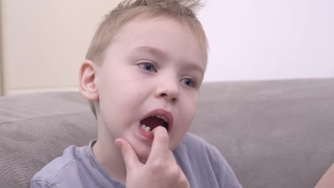 穿着t恤的有趣小男孩在舒适的沙发上放松下颚骨上的乳牙，在明亮的客厅近距离观看。
