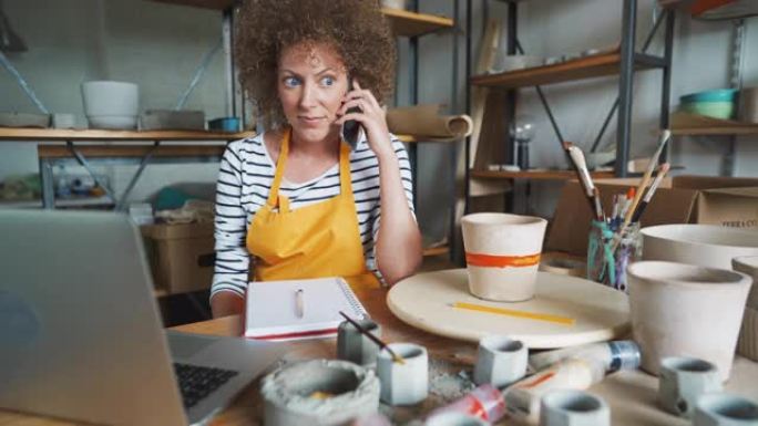 一位手工艺人在她的陶器工作室中使用智能手机和笔记本电脑进行在线订单