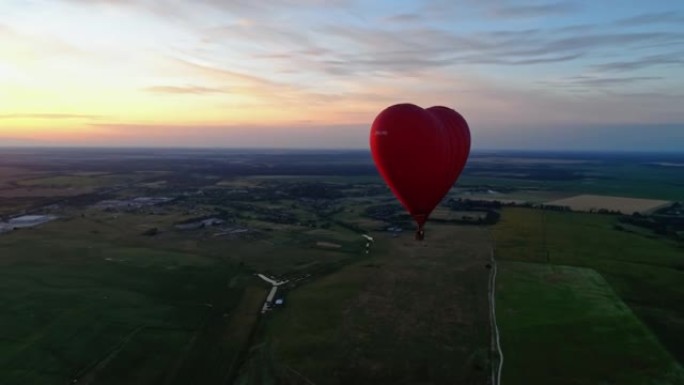 红色浮空器在夕阳下。热气球在乡下的田野上空飞行。心脏形式的热气球。鸟瞰图。