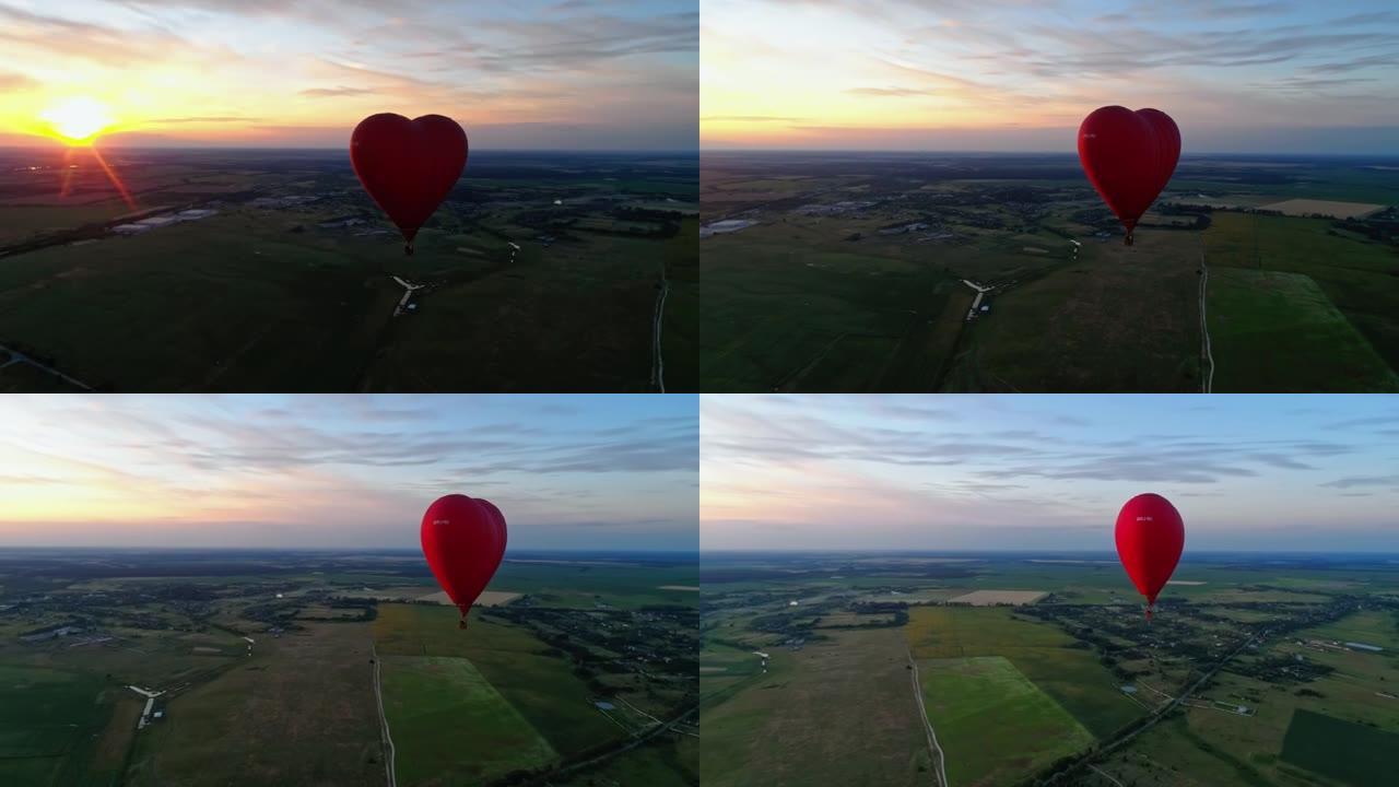 红色浮空器在夕阳下。热气球在乡下的田野上空飞行。心脏形式的热气球。鸟瞰图。