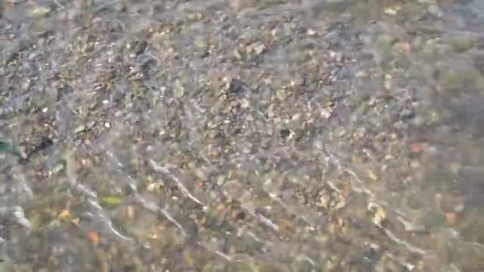 浅溪的底部是彩色的小石头，在晴朗的晴天，它们可以通过清澈的水看到。特写。顶视图。水的催眠运动。4K。