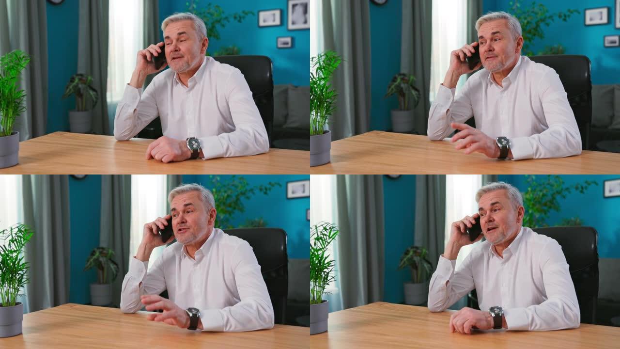 高级白发55岁男子坐在家里拿着智能手机享受愉快的交谈。老一辈人和现代无线技术使用方便舒适，远程通信概