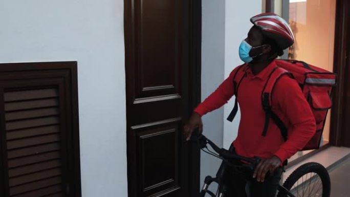 非洲男子用电动自行车送餐 -- 快递员一边为冠状病毒疫情戴安全口罩一边为送餐工作