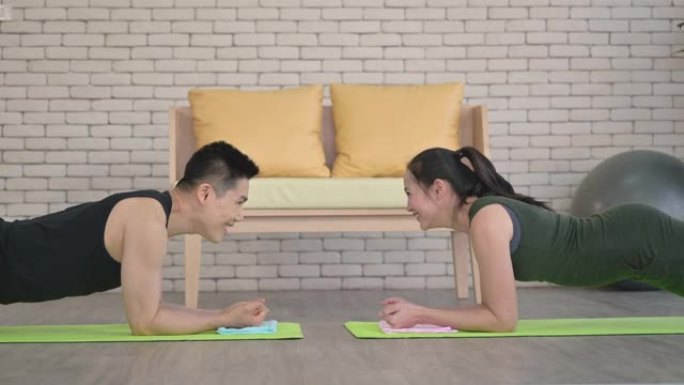 快乐的亚洲夫妇在家里的客厅一起做铺板运动。