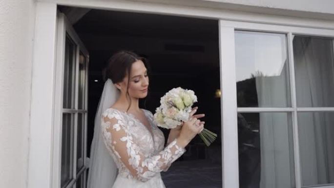 新娘穿着婚纱和面纱，戴着新郎的花束，住在家里阳台门附近