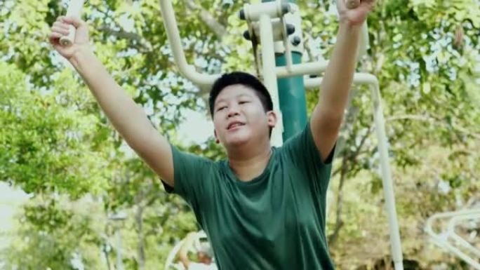 亚洲青春期男孩试图用户外运动器材在公园里用太阳光锻炼，生活方式概念。