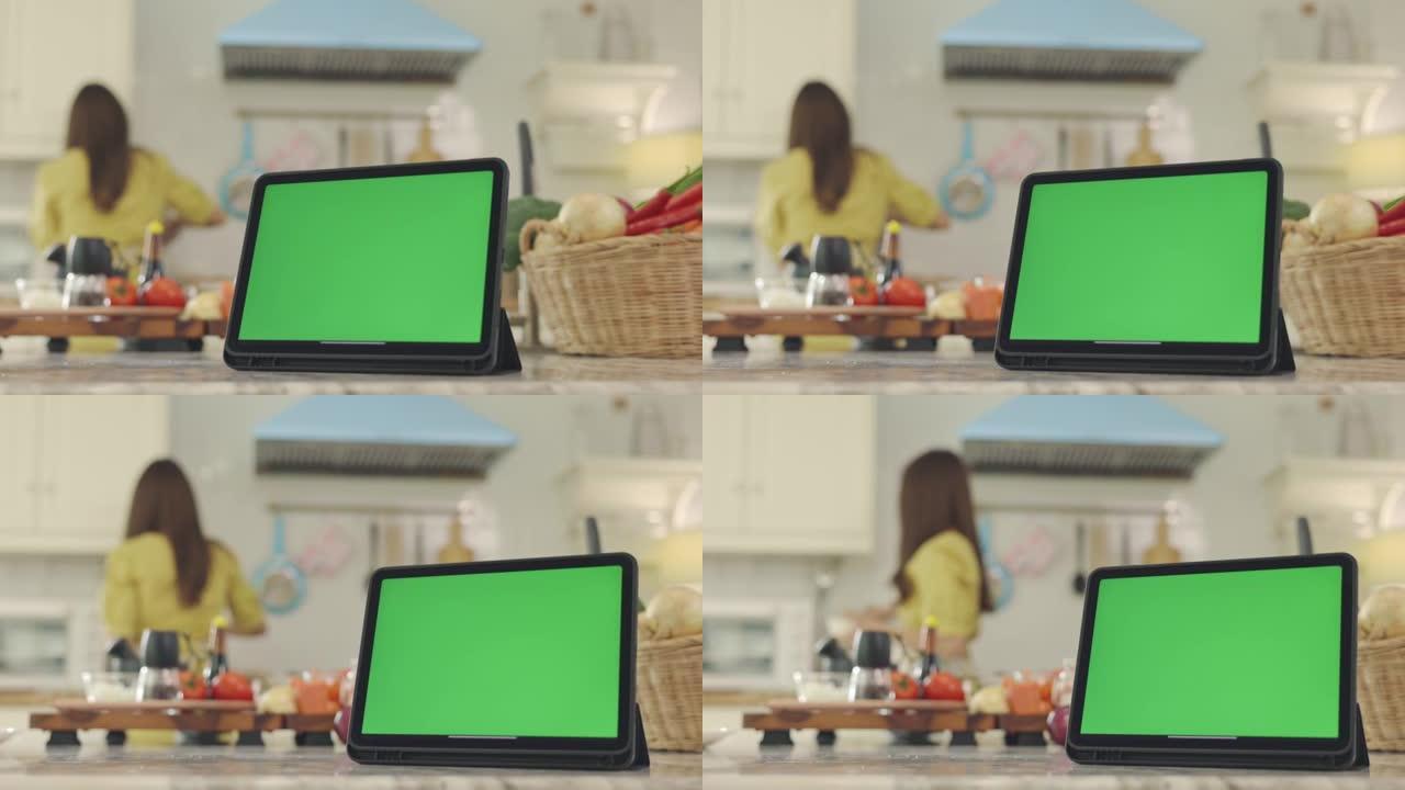 平板电脑带有绿色屏幕，背景优美，在屋子里做饭，带着幸福的脸，妻子在家里开心地做早餐。