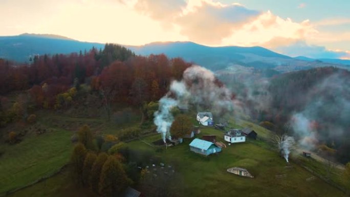 鸟瞰遥远的村庄，在日落时乌克兰喀尔巴阡山脉的秋天森林树木之间的宽阔山丘草地上有小牧羊人的房子。