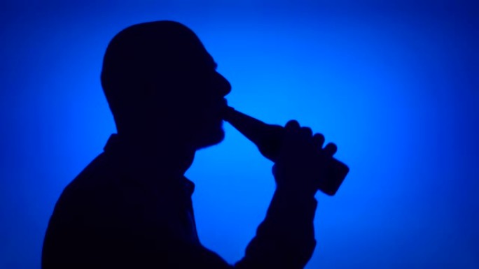 蓝色背景上的高级男子打开啤酒瓶的剪影。男性的脸在侧面喝酒