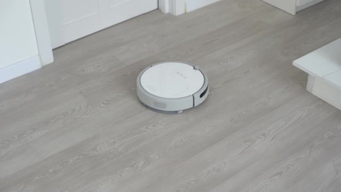 层压地板上的白色机器人真空吸尘器清洁客厅内部的灰尘。智能家政技术。