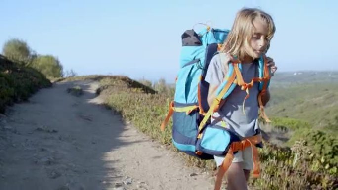 疲惫的女孩走在山路上，背着沉重的大背包