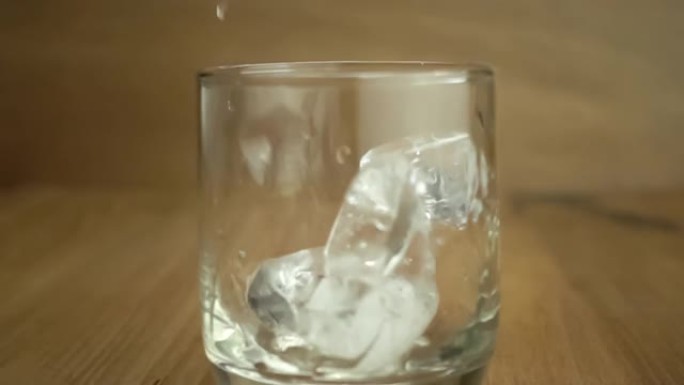 Dropping ice cubes into a transparent glass on woo