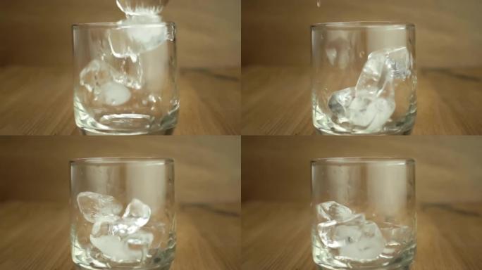 Dropping ice cubes into a transparent glass on woo