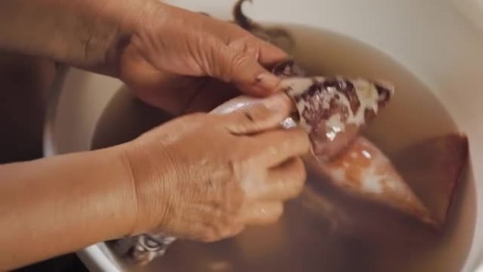 鱿鱼被一位老太太的手剥皮了。洗一下。宏观拍摄。用传统方式准备海鲜餐。