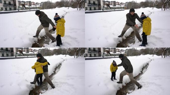 年轻的父亲在雪中帮助儿子越过溪流