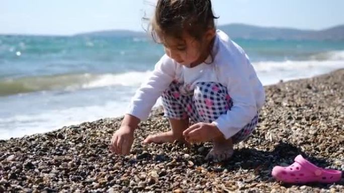小女孩在沙滩上玩鹅卵石，用可爱的方式看着相机。