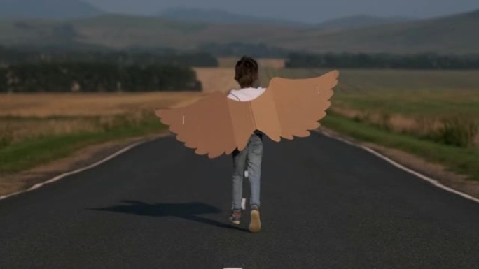 快乐小男孩儿童天使在乡村道路上与玩具纸板飞机翅膀一起奔跑