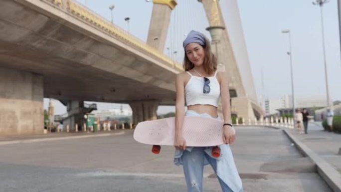 肖像年轻潮人亚洲妇女在公园里拿着滑板