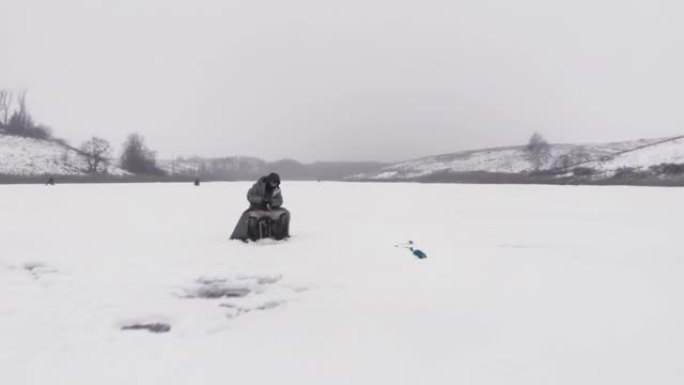 人类独自在冰冻的湖上钓鱼。冬季钓鱼概念。渔夫正在池塘上的冰洞里抓鱼
