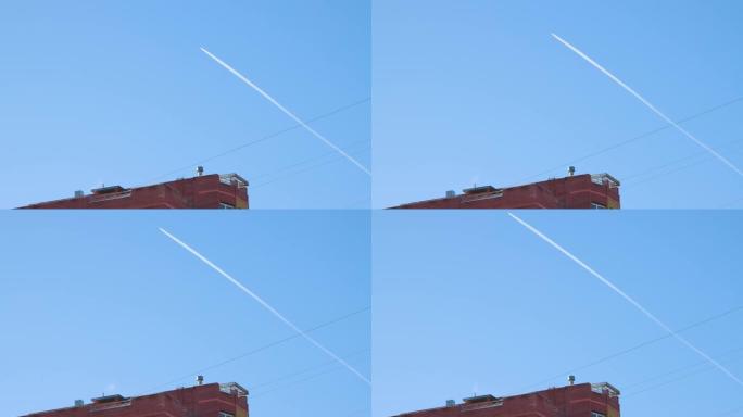 一架飞机飞过一栋高层建筑的屋顶，留下一条白色的小径。