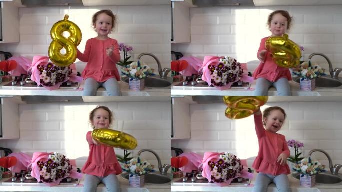可爱的有趣的小女孩拿着金色气球8 8坐在厨房的桌子上，手里拿着一束春花，在家问候母亲或祖母。母亲节。
