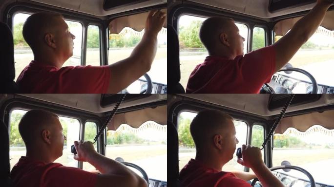 卡车司机在晴天开车时通过无线电通讯讲话。卡车司机骑在乡间小路上，用对讲机说话。物流和运输的概念。关闭