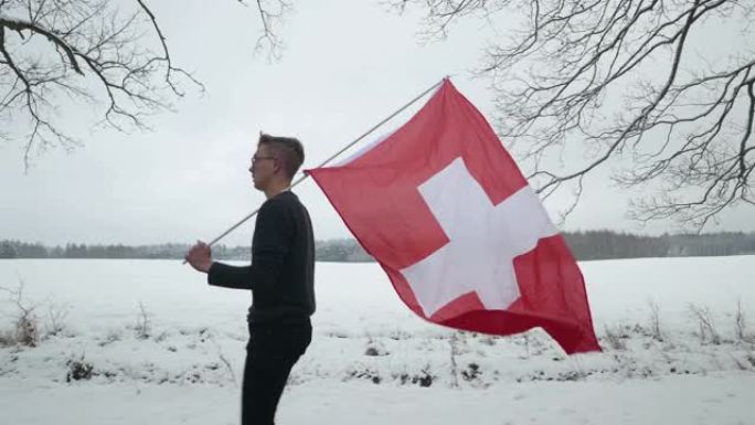 一个年轻人举着瑞士国旗在雪地里奔跑