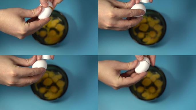 雄性手拿着一个破裂的鸡蛋。把鸡蛋打碎在杯子上。蓝色背景。慢动作