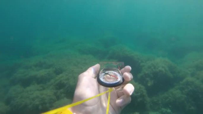 持塑料磁性罗盘的男性手的第一人称视角从侧面旋转，并在水下寻求正确的方向。