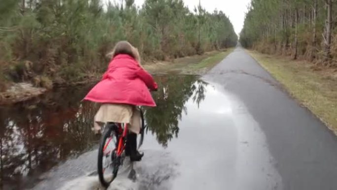 漂亮的年轻女孩在洪水泛滥的小路上骑自行车