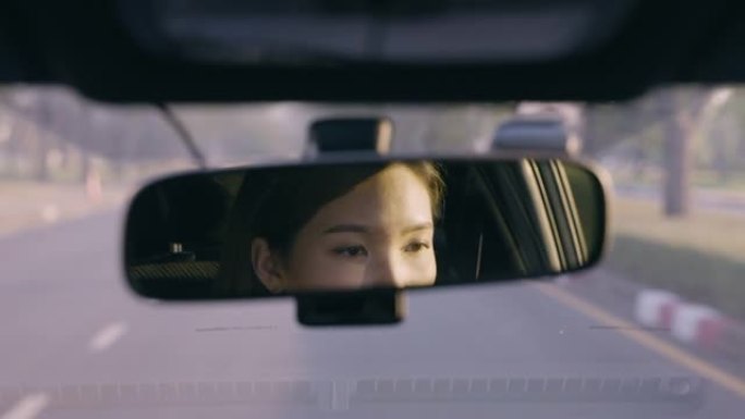 特写镜头亚洲女子驾驶汽车在道路上倒映在后视镜中
