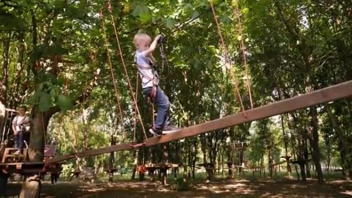 勇敢的小男孩在冒险公园的树木之间通过电缆路线。