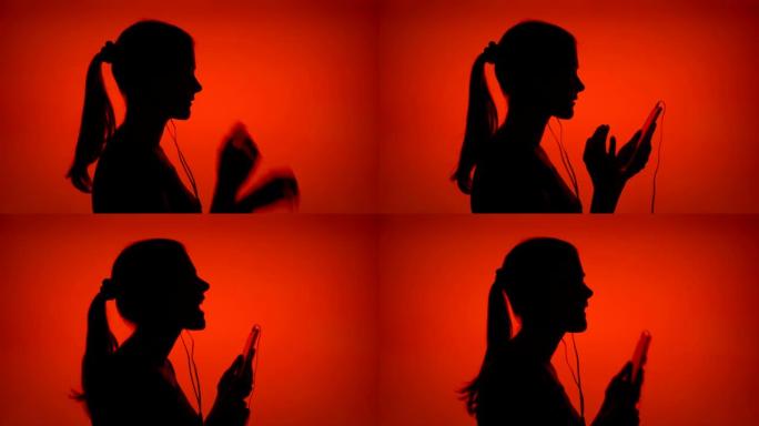 年轻女子的剪影戴上耳机，在红色背景的智能手机上听音乐