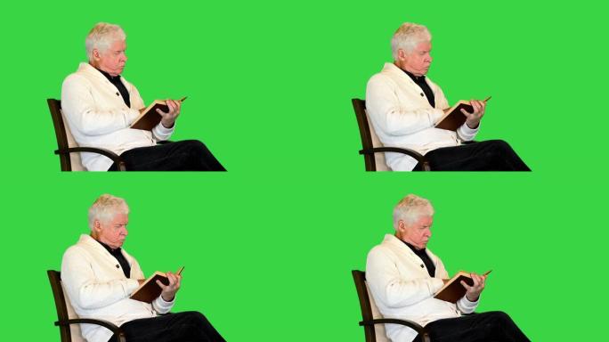 高年级男子坐在绿色屏幕上的椅子上学习一本书，色度键