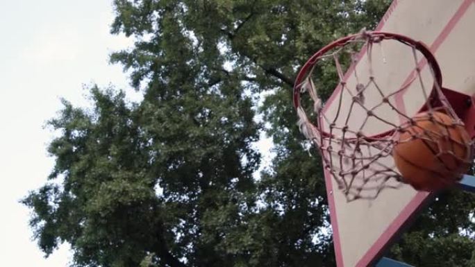 投掷的橙色篮球干净地击中了树荫下的室外球场上的篮筐。击中目标。用干净的慢动作达到目标