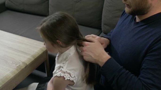 中年男子试图把他小女儿的辫子编成辫子。他不擅长这个。孩子生气了