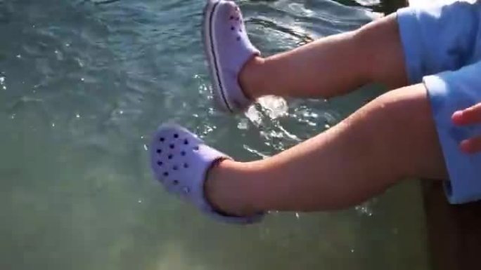 穿着紫色鞋子的小孩在喷泉水中摆动腿