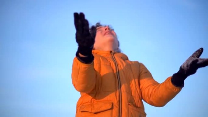 冬天快乐少年在雪地上玩耍的肖像。冬天在蓝天背景下特写卷发男孩的肖像。孩子戴着手套扔雪