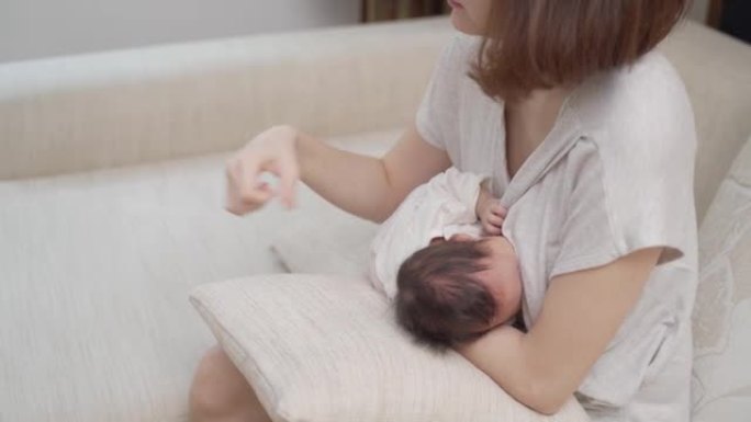 亚洲女性母亲抱着婴儿喂母乳，有手腕疼痛的征兆和症状。拥抱孩子造成的手腕肌腱损伤。女性母亲患有健康问题