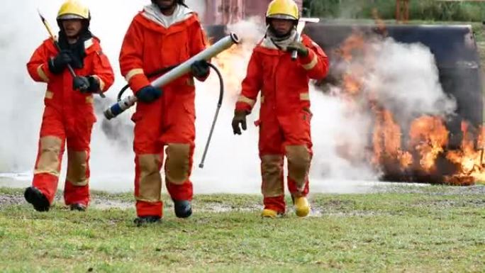 消防队员用消防水龙带灭火，使用化学水和泡沫喷雾机灭火。消防队员戴安全帽，穿安全服制服。消防灭火器的救