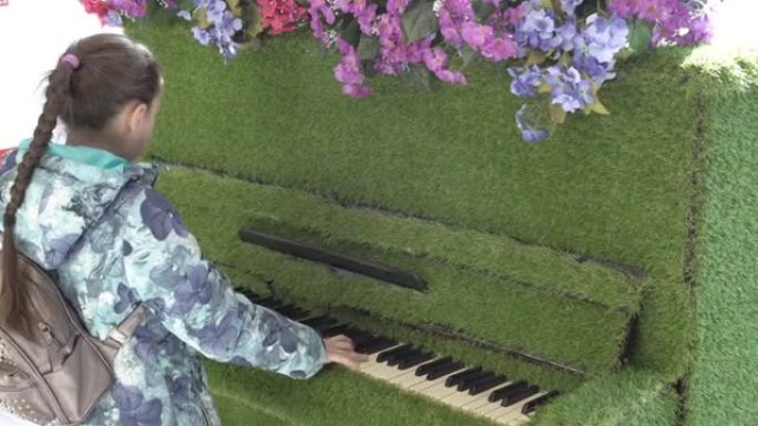 一个年轻的女孩，一个少年，穿着外套，弹钢琴，钢琴站在公共场所。钢琴上装饰着鲜花和绿色植物。特写。后视