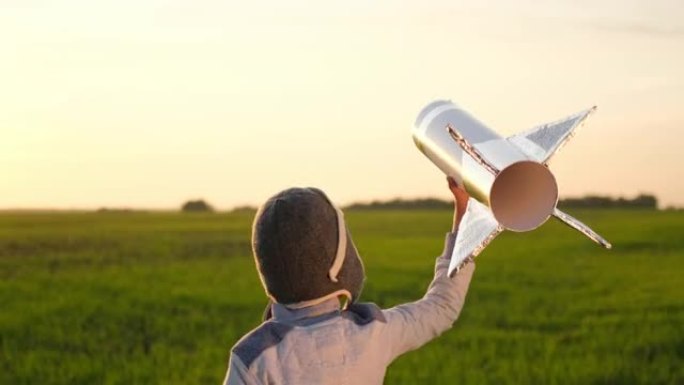 快乐的小男孩头盔飞行员宇航员在日落野外夏季大自然中与玩具火箭同行。孩子大梦想飞行，宇航员，太空，成功