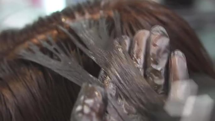 理发师手上的特写镜头。大师在一家美容院用黑色画女孩的头发