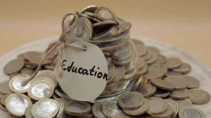 孤立的橙色背景上的一堆硬币，旋转着教育铭文的玻璃罐。学习和知识的预算计划和收益投资，储蓄和赚钱策略