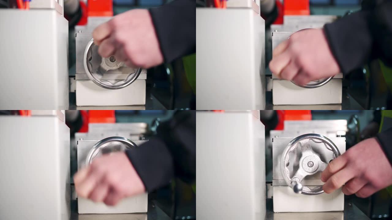 一名男工人在机器上转动轮子以滚动橡胶混合物的特写视图