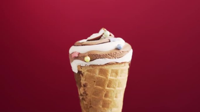 巧克力冰淇淋蛋卷在红色背景上旋转。五颜六色的糖洒在美味的自制咖啡冰淇淋上。